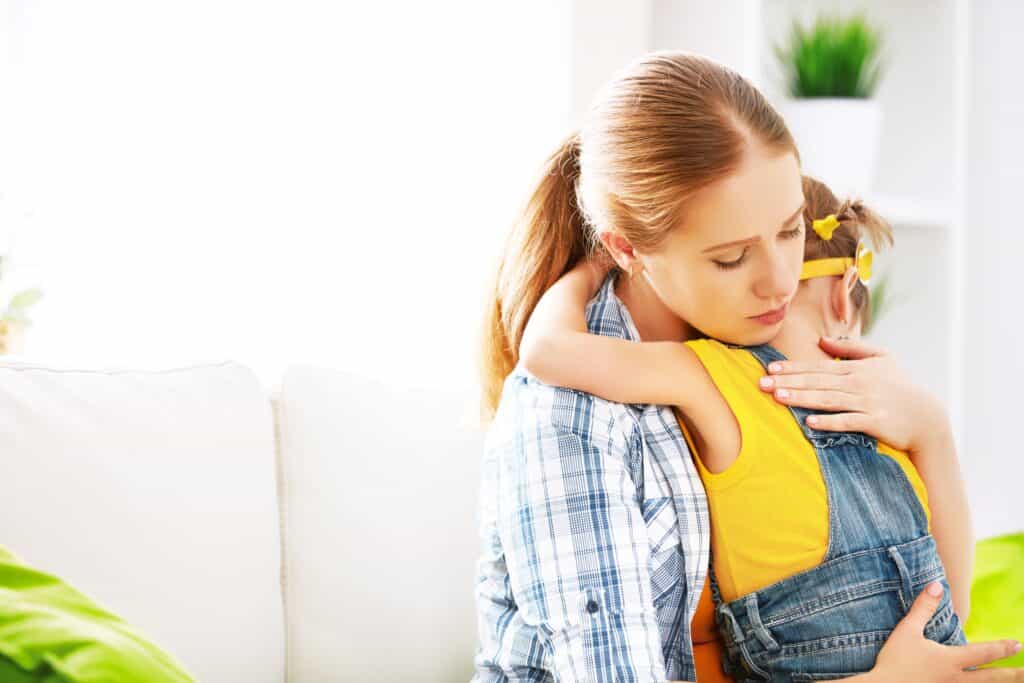 An adult parent embraces a child with a pouty face in a comforting hug, as a way of expressing empathy and understanding.